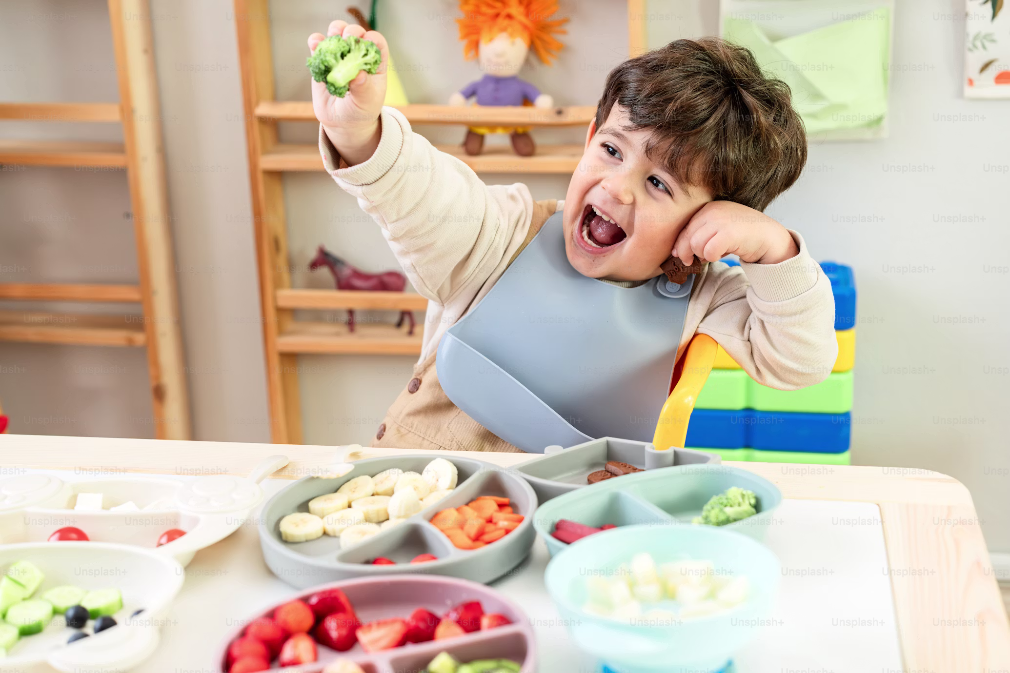 Toddler cheering with a piece of broccoli at the table