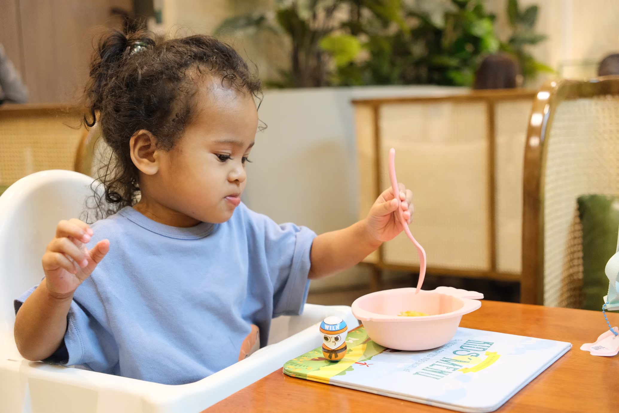 Toddler feeding herself with a spoon in a high chair